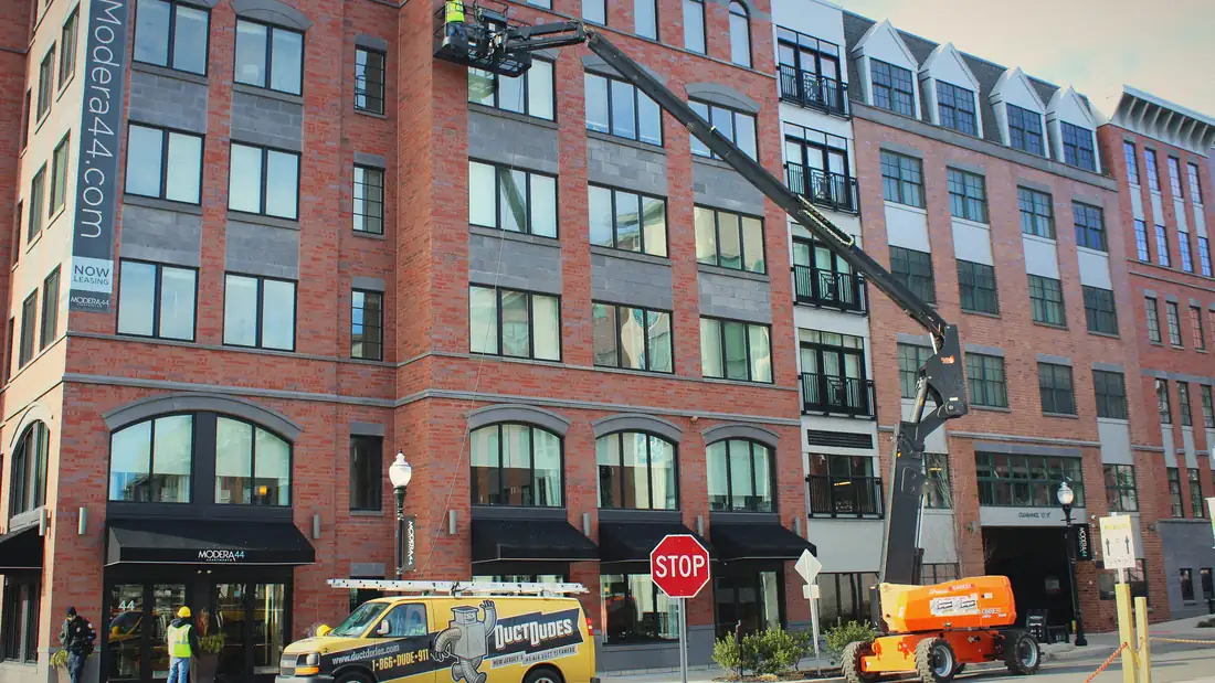 Duct Dudes van and boom lift cleaning dryer vents on a six-story apartment building
