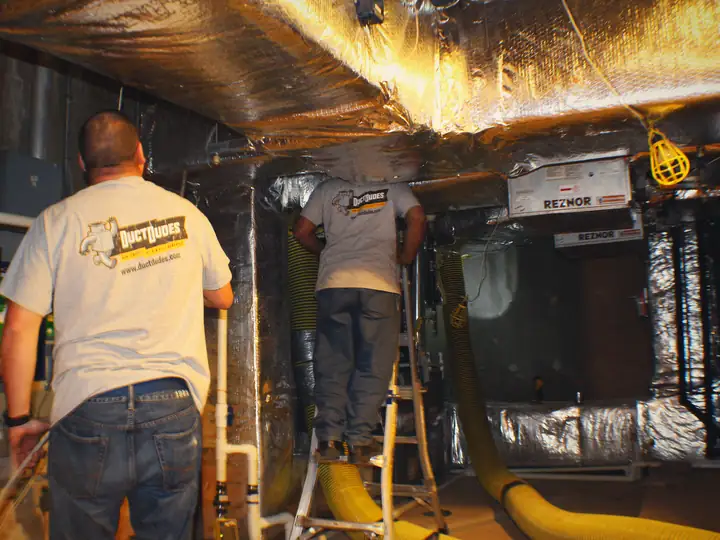 Two Duct Dudes technicians cleaning ductwork in a commercial mechanical room